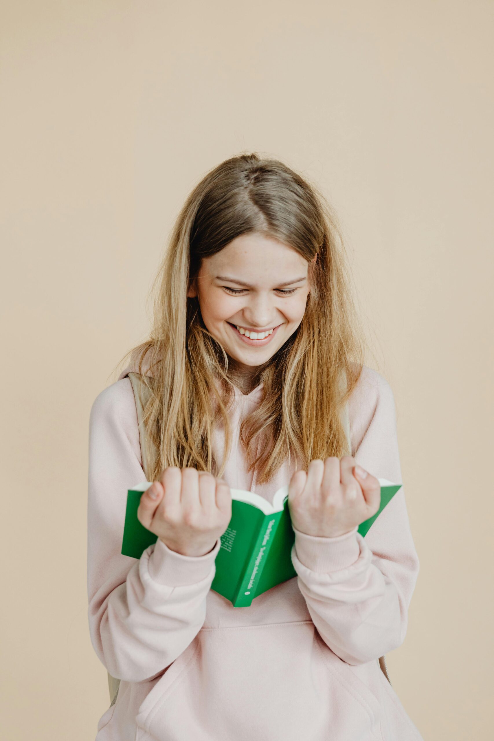 Teenage girl smiling and reading a book, conveying happiness and education focus.